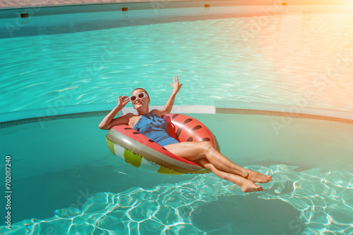 Happy woman in a swimsuit and sunglasses floating on an inflatable ring in the form of a watermelon, in the pool during summer holidays and vacations. Summer concept. © svetograph