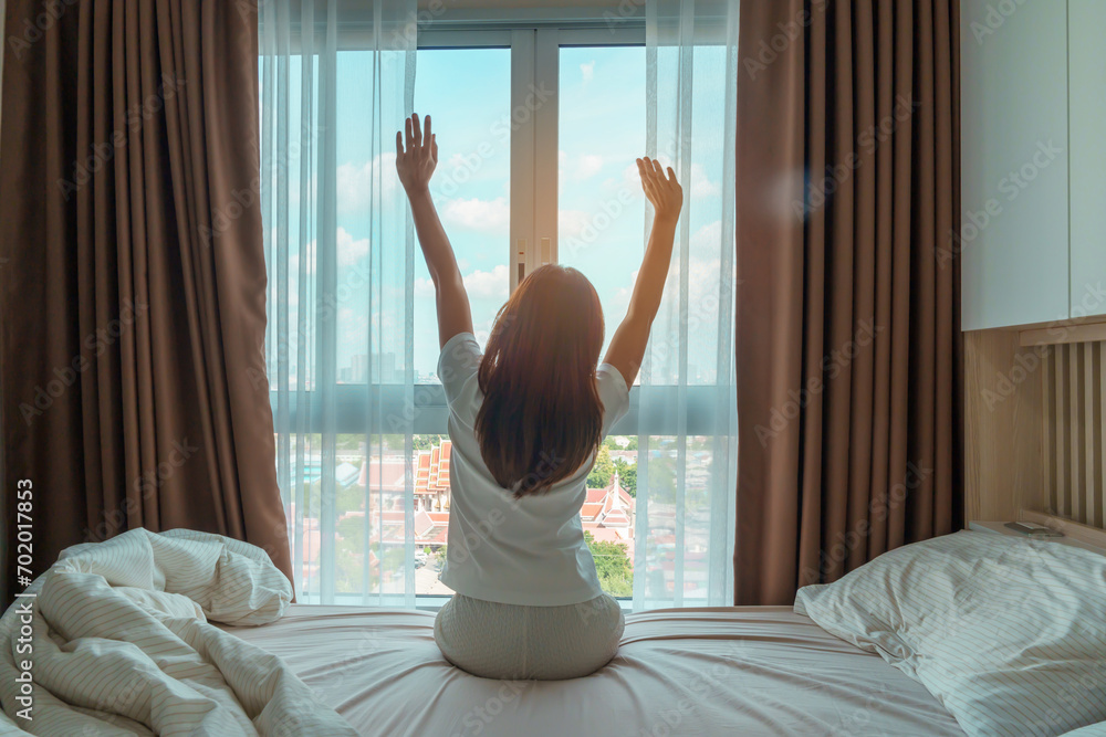 happy woman stretching on bed after wake up, young adult female rising arms and looking to window in the early morning. fresh relax and have a nice day concepts - obrazy, fototapety, plakaty 