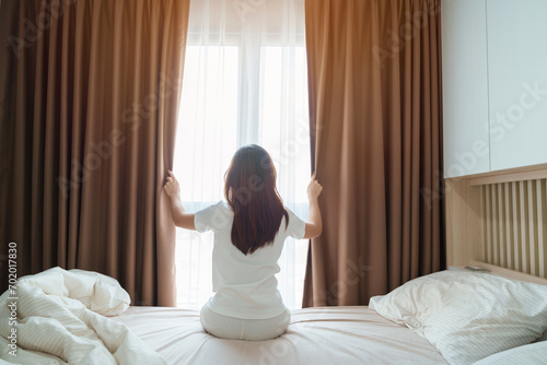 happy woman stretching on bed after wake up, young adult female rising arms and looking to window in the early morning. fresh relax and have a nice day concepts