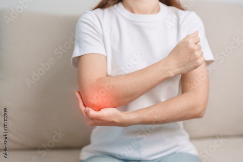 Woman having elbow ache during sitting on couch at home, muscle pain due to lateral epicondylitis or tennis elbow. injury, Health and medical concept photo