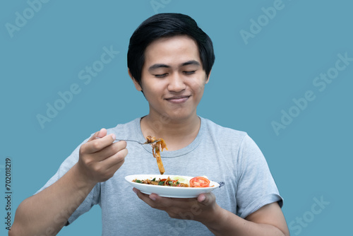 A man in a gray shirt is holding a fork and a plate containing food, for design and visual editing purposes. photo