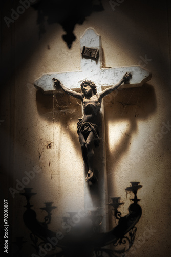 Crucified Jesus Christ figure in a ray of sunlight in a grave with spider webs hanging on him, very moody backdrop  photo