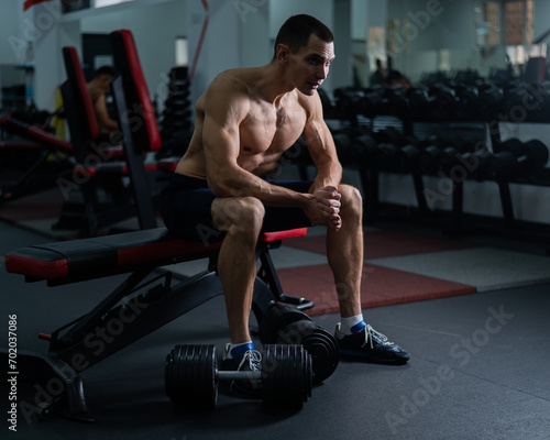 Muscular shirtless man sitting on a bench and resting after a workout. 
