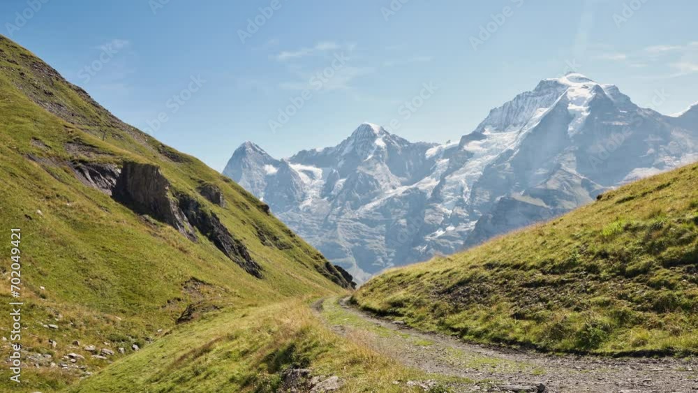 A tourist captured an image of roads in the valley covered with grass, with snow-covered mountains in the background A tourist captured an image of roads in the valley covered with grass, with snow-covered mountains in the background