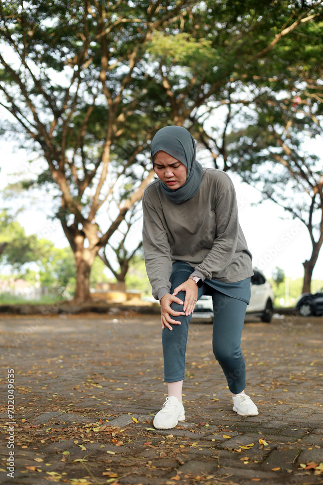 Joint pain, Arthritis and tendon problems. an asian muslim woman touching knee at pain point in the park