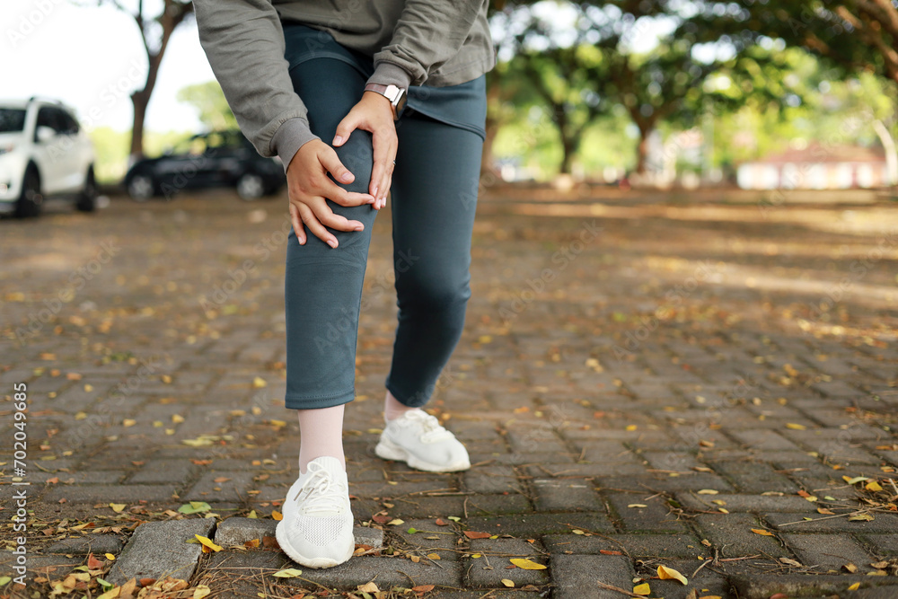 Fototapeta premium Joint pain, Arthritis and tendon problems. an asian muslim woman touching knee at pain point in the park. Close up photo