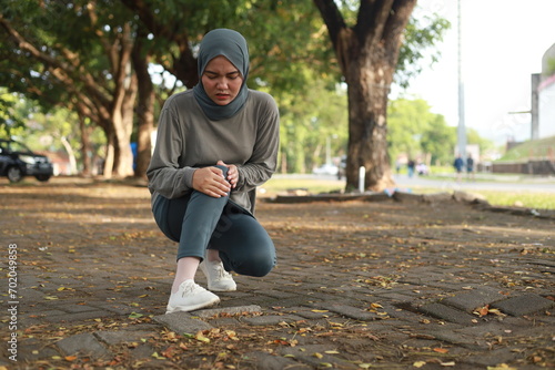 Joint pain, Arthritis and tendon problems. an asian muslim woman touching knee at pain point in the park