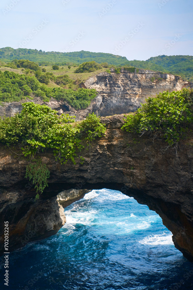 Rock broken by an ocean wave forming an arch in the mountain. Cliff is washed by powerful waves of ocean. Angel's Billabong is a popular tourist destination on the island of Nusa Penida in Indonesia.
