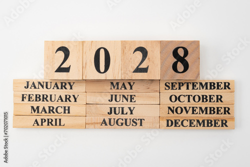 Year 2028 written on wooden cubes on top of the months of the year written on twelve rectangular pieces of wood. Isolated on white background