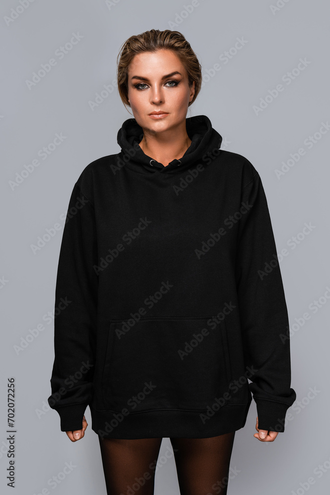 Woman dressed in a black oversized hoodie with blank space, ideal for a mockup, set against gray background