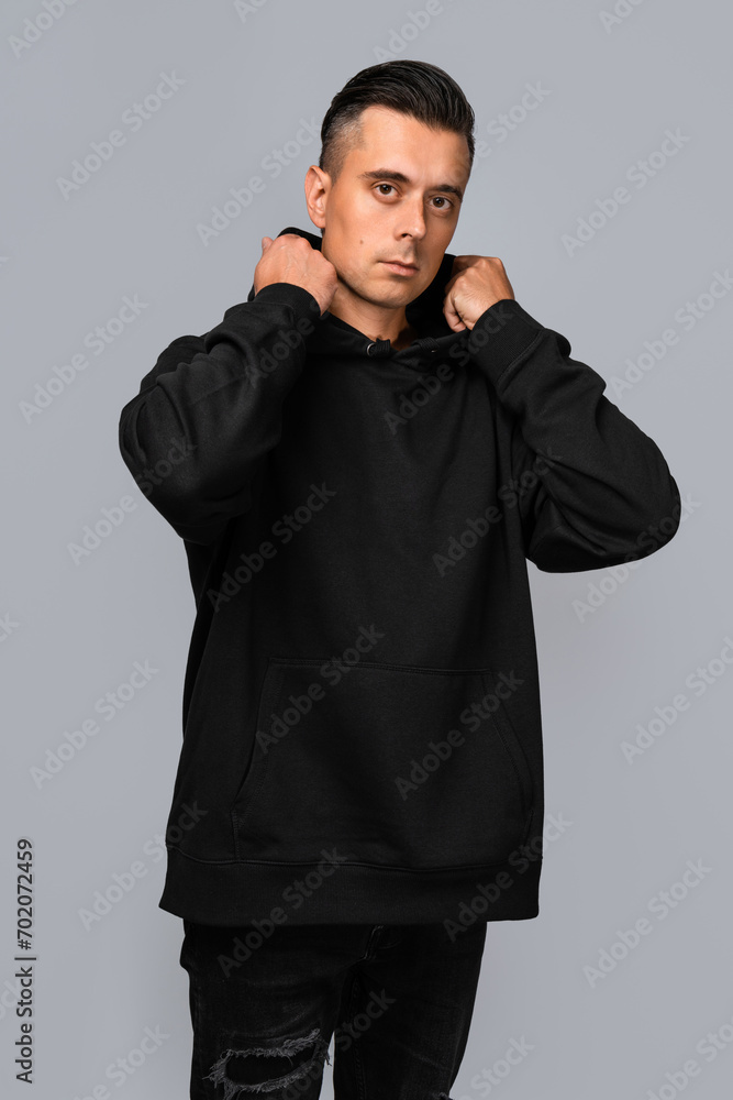 Man dressed in a black oversized hoodie with blank space, ideal for a mockup, set against gray background Man dressed in a black oversized hoodie with blank space, ideal for a mockup, set against gray background