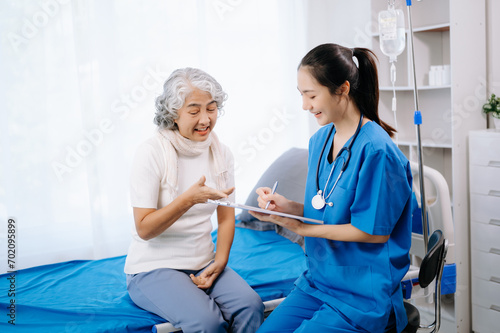 Doctor and Asian elderly patient who lie on the bed while checking pulse, consult and explain with nurse taking note in hospital wards.