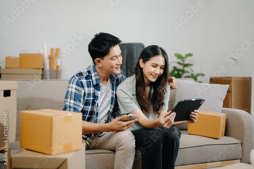 Young attractive couple man and woman use tablet and smartphone online shopping furniture decorate house with carton package move in new house. ฃ.