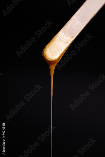 liquid golden wax or sugar paste for depilation drains from the stick on black background. depilation, waxing, sugaring smooth skin, beauty, cream, banner, black color