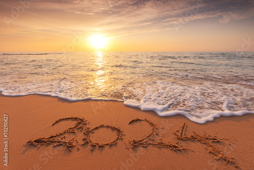 Sunrise over the sea waves and text 2024 happy new year written on island beach sand 