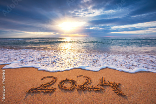 Sea sunrise over tropical island beach and handwritten text in sand new year 2024