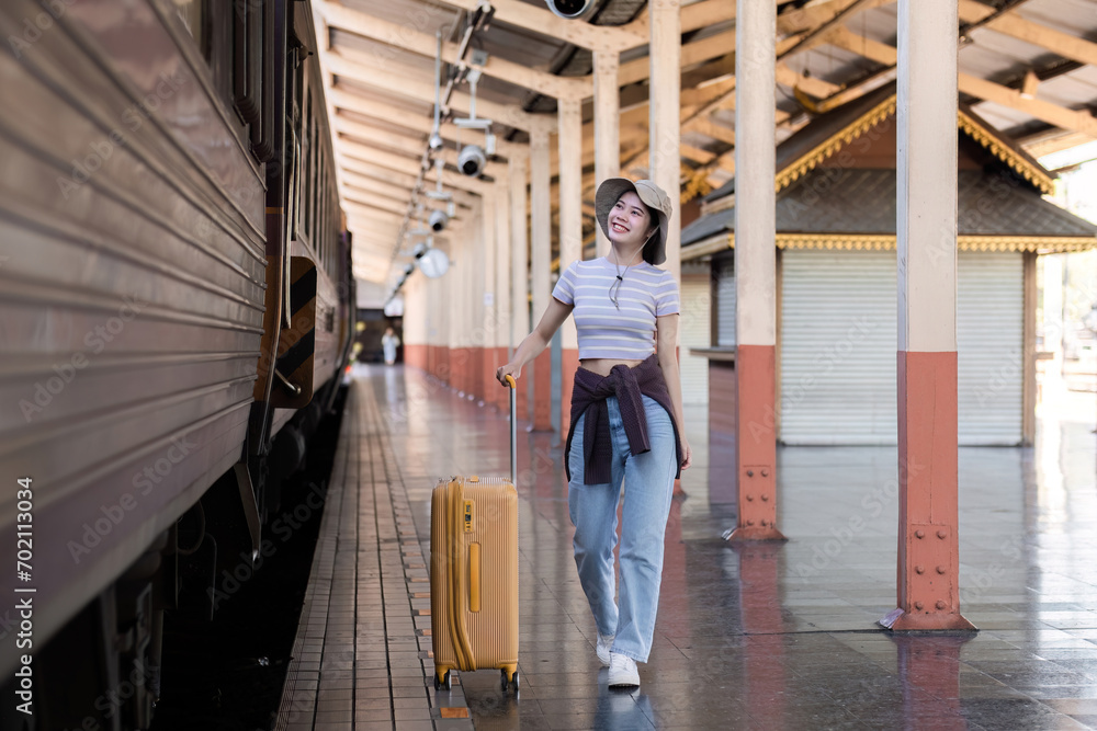 Young woman wearing an explorer's hat and carrying a suitcase Stand and look for a train at the train station. Traveler's concept