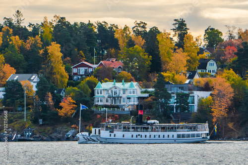 Stockholm, Sweden. Suburbs and residential houses on the islands east of the city in autumn colors. A commuter boat passing by. Colorful trees. photo