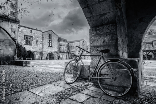 Black and white image of a bicycle under the covered walkway surrounding the market square of the 13th century bastide of Monpazier in the Dordogne region of France photo