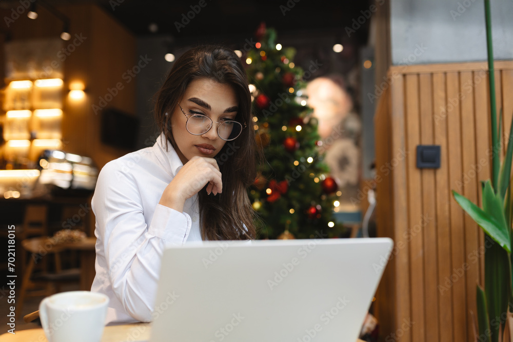 Photo of shiny positive woman with glasses sitting cafeteria drinking coffee and using her laptop for freelance work or online meeting Photo of shiny positive woman with glasses sitting cafeteria drinking coffee and using her laptop for freelance work or online meeting