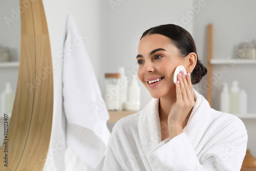 Beautiful woman removing makeup with cotton pad near mirror in bathroom, space for text photo