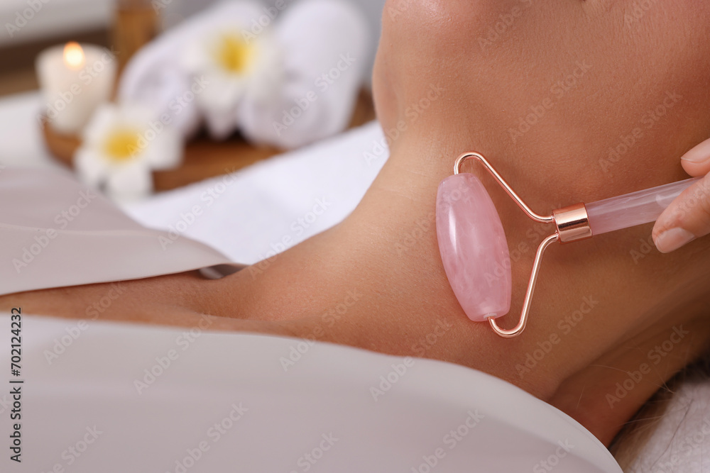 Naklejka premium Woman receiving facial massage with rose quartz roller in beauty salon, closeup