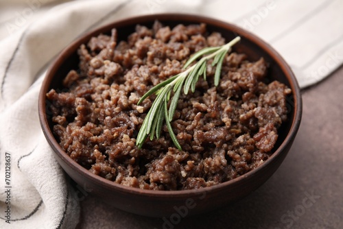 Fried ground meat in bowl and rosemary on brown textured table, closeup