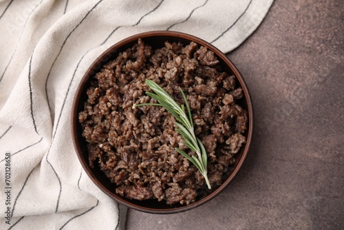 Fried ground meat in bowl and rosemary on brown textured table, top view photo