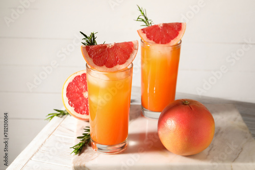 Tasty grapefruit drink with ice in glasses  rosemary and fresh fruits on light wooden table