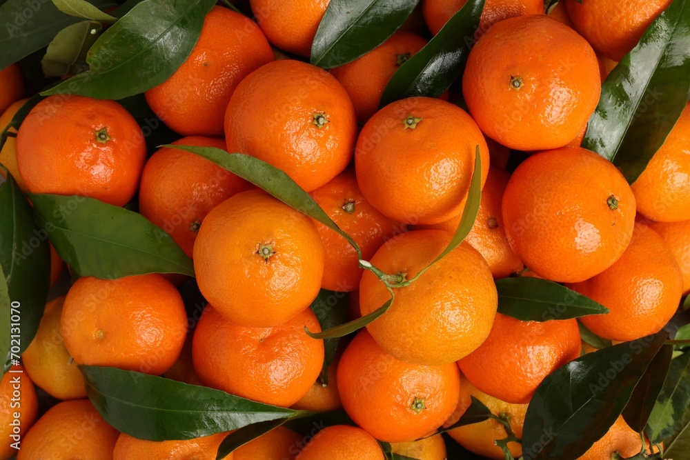 Delicious tangerines with leaves as background, top view
