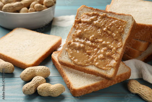 Delicious toasts with peanut butter and nuts on light blue wooden table, closeup