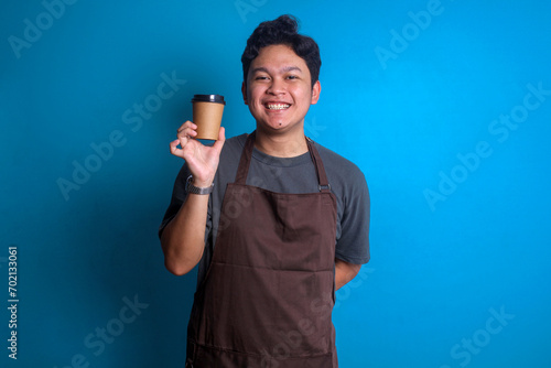 Young Asian barista man wear brown apron hold craft paper brown cup coffee to go
