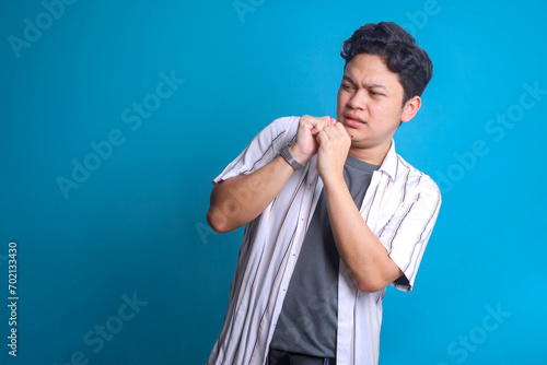 Young Asian man feeling afraid over blue background