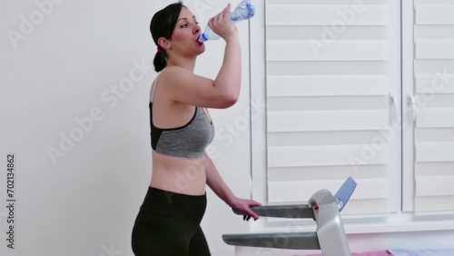 Wallpaper Mural Young woman is exercising on a treadmill and drinking water to hydrate her body, Video Clip 4K  Torontodigital.ca