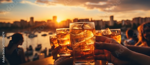 Group of people's hands toasting with a glass of drink at sunset. Close up shot. photo