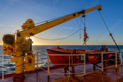 Orange rescue boat on big cargo vessel and crane. Man over board drill. Lifeboat training.