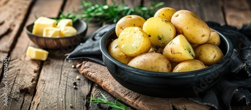 Boiled hot potatoes with steaming in a black bowl and butter served on wooden table ready to eat. with copy space image. Place for adding text or design
