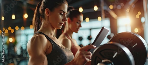 A female personal trainer is tracking progress on tablet while sportswoman is lifting weights in a gym. with copy space image. Place for adding text or design
