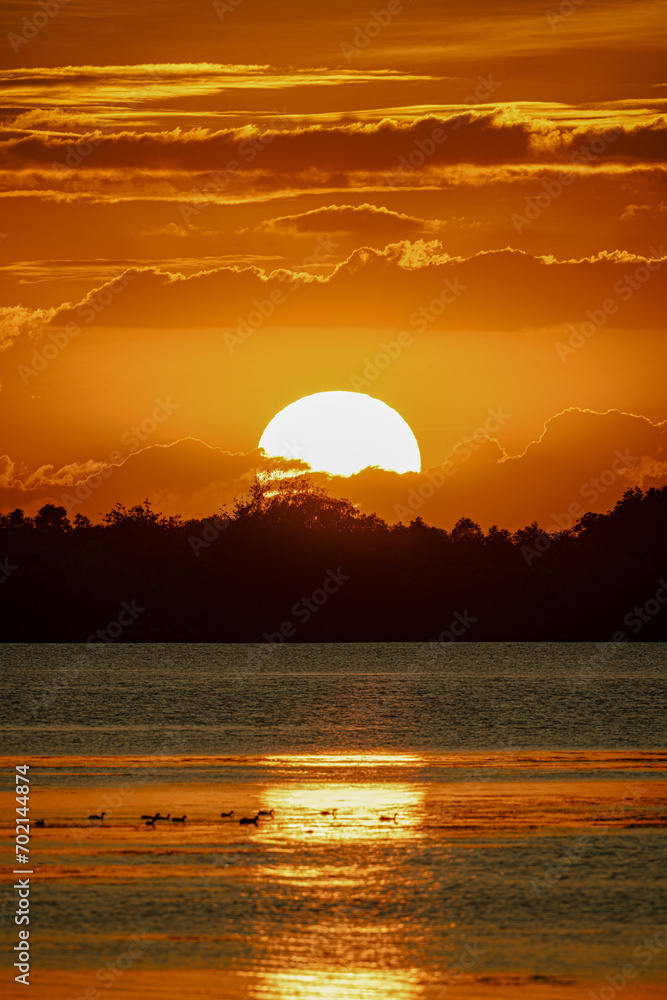 Sunset at the river. Nature landscape. The sun below the horizon, a fiery glow over the peaceful lake. The water sparkled with the sunset's colors, reflecting nature's beauty. Orange summer sunset