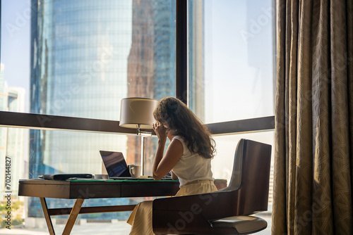 Tired businesswoman freelancer working with laptop and she is sitting on the chair, window with panoramic view in the city background. Low key photo