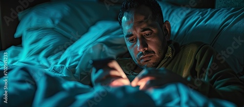 A bored hispanic man watching videos on his cellphone while half asleep lying on the bed in his room. with copy space image. Place for adding text or design photo