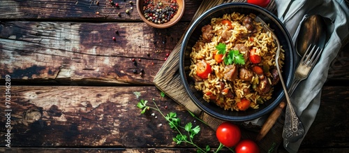 Fragrant pilaf with meat and vegetables close up on a plate Top view on wooden table Fork knife and towel. with copy space image. Place for adding text or design