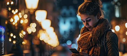 Crop female in warm scarf standing near illuminated lamps in dark street and typing message on phone during walk time. with copy space image. Place for adding text or design