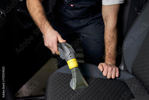 Car seat vacuum  car detailing and cleaning of interior seats at luxury modern cars. Close-up photo. Cropped auto mechanic cleaning inside of car  vacuuming