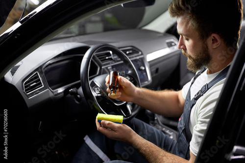 young car wash service worker cleaning car interior with special chemical anti dust liquid. side view on male holding bottle with liquid in hands applying it on rag. side view, copy space