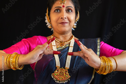 Beautiful Indian female classical dancer performing Bharatanatyam postures on black background