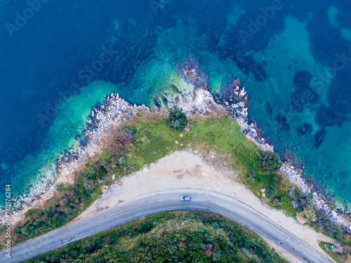 Aerial view of road between green summer forest and blue beach. car moving on road.