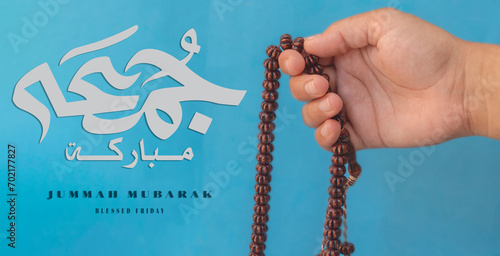 Jummah Mubarak blessed happy Friday Arabic calligraphy, Selective focus image hand of Muslim woman holding prayer beads.