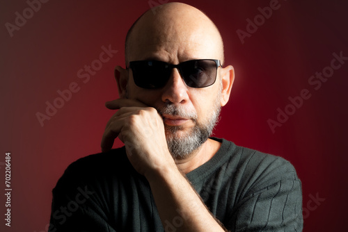 White, bald man, wearing sunglasses, confident and serious looking towards the camera.