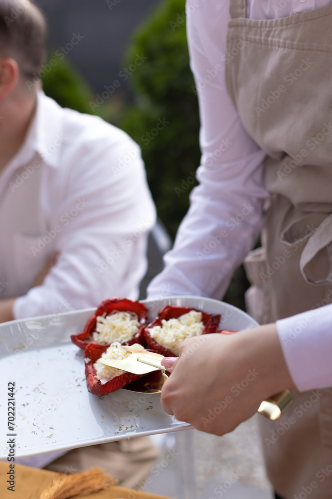 Baked red-colored bell peppers stuffed with herbs and cheese on a dish on summer outdoors party Baked red-colored bell peppers stuffed with herbs and cheese on a dish on summer outdoors party